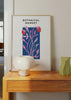 Gerahmtes Wandbild mit botanischer Komposition aus rosa Stielen und Früchten, kräftigem blauem Hintergrund, schwarzer Typografie und zeitgemäßem Illustrationsstil mit editorischer Anmutung. Erhältlich auf kudeko.com