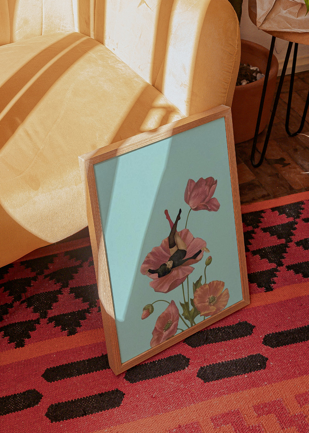 Gerahmtes Wandbild mit liegender Frau zwischen rosa Mohnblumen, hellblauem Hintergrund, grünen Stängeln und surrealer Komposition im Illustrationsstil. Erhältlich auf kudeko.com