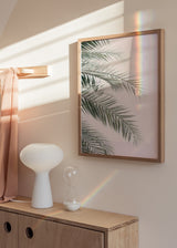 Quadro emoldurado com folhas de palmeira em tons de verde acinzentado sobre fundo rosa envelhecido, composição leve e estilo natureza e paisagem. Disponível em kudeko.com