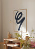 Gerahmtes Wandbild mit großer abstrakter Form in geschwungener marineblauer Linie auf cremeweißem Hintergrund, fließende Komposition im modernen und eleganten Stil. Erhältlich auf kudeko.com