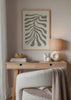 Tableau encadré avec branche botanique aux formes organiques allongées en gris taupe sur fond beige clair, dans un style minimaliste et épuré. Disponible sur kudeko.com
