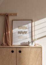 Gerahmtes Wandbild mit drei übereinanderliegenden wellenförmigen Flächen in Beige, Taupe und Elfenbein auf weißem Hintergrund, klare Komposition im minimalistischen Stil. Erhältlich auf kudeko.com