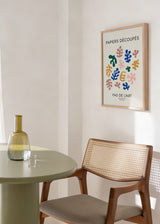 Tableau encadré avec formes de feuilles découpées en bleu, vert, moutarde et rose poudré sur fond crème, typographie noire et style abstrait contemporain. Disponible sur kudeko.com