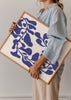 Wandbild mit abstrakter botanischer Komposition aus blauen Blättern und Stängeln auf cremeweißem Hintergrund, mit fließenden organischen Formen und klarem modernem Stil. Erhältlich auf kudeko.com