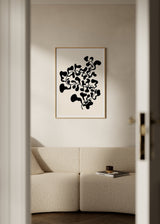 Wandbild mit abstrakter Pflanze, feinen Zweigen und schwarzen organischen Blättern auf cremefarbenem Hintergrund, im minimalistischen zeitgenössischen Stil. Erhältlich auf kudeko.com