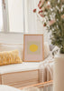 Quadro emoldurado com sol circular amarelo centrado, fundo bege e rosa poudre, composição depurada de estilo minimalista e contemporâneo. Disponível em kudeko.com