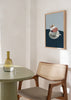 Tableau encadré avec femme allongée sur un lit dans une tasse à café blanche, fond bleu clair, table bleu marine et style vintage délicat. Disponible sur kudeko.com