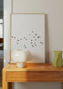 Gerahmtes Wandbild mit schwarzem Vogelschwarm im Flug auf weitem weißem Hintergrund, elegantem Kontrast, luftiger Komposition und minimalistischem Stil. Erhältlich auf kudeko.com