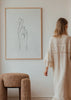 Gerahmtes Wandbild mit Hand und gekreuzten Fingern in feinen schwarzen Linien, auf strukturiertem beigem Hintergrund, im minimalistischen und zeitgenössischen Stil mit ruhigen Naturtönen. Erhältlich auf kudeko.com