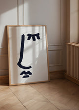 Gerahmtes Wandbild mit abstraktem blauschwarzem Symbol auf weißem Hintergrund, breiten Strichen, lockeren Formen und minimalistischem Stil. Erhältlich auf kudeko.com