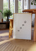 Quadro emoldurado com a palavra HOME em letras pretas dispostas na diagonal, pequeno ícone de casa, fundo branco e estilo minimalista simples e moderno. Disponível em kudeko.com