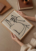 Wandbild mit weiblicher Silhouette in schwarzen Linien auf hellbeigem Hintergrund, mit Oberkörper, Lippen und Hand in eleganter minimalistischer Komposition im modernen Stil. Erhältlich auf kudeko.com