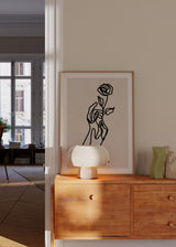 Gerahmtes Wandbild mit einer Hand, die eine Rose hält, in schwarzen Linien auf hellbeigem Hintergrund, minimalistisch, floral, modern und elegant gestaltet. Erhältlich auf kudeko.com