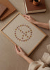 Cuadro decorativo de estilo minimalista y ilustración colocado en dormitorio, símbolo de paz con flores en tonos suaves, modelo Símbolo Paz Flores
