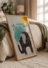 Quadro emoldurado com elefante preto de formas simples, mancha turquesa, sol amarelo e laranja, fundo claro e estilo infantil moderno. Disponível em kudeko.com