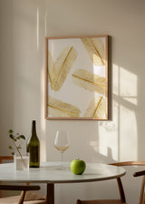 Gerahmtes Wandbild mit länglichen tropischen Blättern in Gold auf weißem Hintergrund, leichte, helle und klare Komposition im minimalistischen Stil für moderne Räume. Erhältlich auf kudeko.com