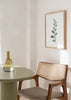 Tableau encadré avec fine branche de feuilles allongées vert sauge et gris vert sur fond blanc, dans un style minimaliste et apaisant. Disponible sur kudeko.com