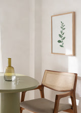 Tableau encadré avec fine branche de feuilles allongées vert sauge et gris vert sur fond blanc, dans un style minimaliste et apaisant. Disponible sur kudeko.com