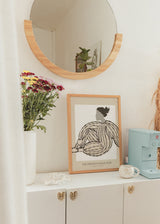 Gerahmtes Wandbild mit sitzender weiblicher Figur, Kleid mit schwarzen Streifen, beigem und weißem Hintergrund, organischen Formen und minimalistischem Stil in neutralen Tönen. Erhältlich auf kudeko.com