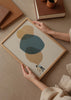 Gerahmtes Wandbild mit zwei Kindern von hinten unter großen überlagerten organischen Formen in Graublau, Beige und auf hellem Hintergrund, im zeitgenössischen und ruhigen Illustrationsstil. Erhältlich auf kudeko.com