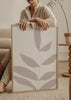 Gerahmtes Wandbild mit Zweig und länglichen Blättern in Rosébeige auf weißem Hintergrund, dezenter Sprenkelstruktur und klarem minimalistischem Stil. Erhältlich auf kudeko.com