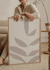 Gerahmtes Wandbild mit Zweig und länglichen Blättern in Rosébeige auf weißem Hintergrund, dezenter Sprenkelstruktur und klarem minimalistischem Stil. Erhältlich auf kudeko.com