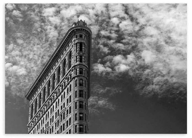 Horizontales Wandbild eines klassischen Gebäudes an schmaler Ecke, in Untersicht fotografiert, mit dramatischem Wolkenhimmel in Grau, Schwarz und Weiß, im urbanen architektonischen Stil. Erhältlich auf kudeko.com