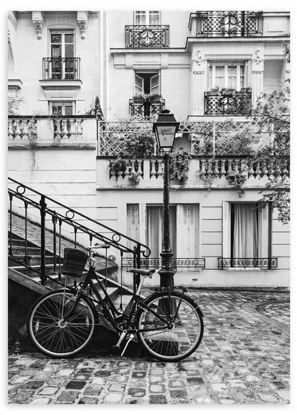 Quadro emoldurado de rua parisiense a preto e branco com bicicleta, candeeiro, varandas clássicas, escadaria em ferro forjado, fachadas antigas e estilo fotográfico urbano. Disponível em kudeko.com