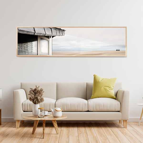 Quadro horizontal com o canto de uma construção junto a uma praia vazia, céu suave azul acinzentado, areia clara e composição panorâmica de estilo fotográfico. Disponível em kudeko.com