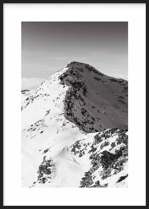 Wandbild mit schneebedecktem Berg, dunklen felsigen Graten, sanft grauem Himmel sowie weißen, grauen und schwarzen Tönen im sachlichen fotografischen Stil. Erhältlich auf kudeko.com