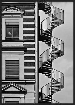 Tableau représentant une façade urbaine en noir et blanc avec escalier en colimaçon extérieur, fenêtres classiques, lignes architecturales nettes et silhouette solitaire, dans un style photographique contemporain. Disponible sur kudeko.com