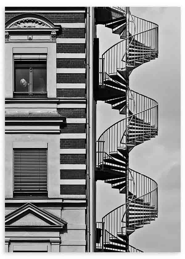 Cuadro de fachada urbana en blanco y negro con escalera de caracol exterior, ventanas clásicas, líneas arquitectónicas marcadas y figura solitaria, de estilo fotográfico. Disponible en kudeko.com