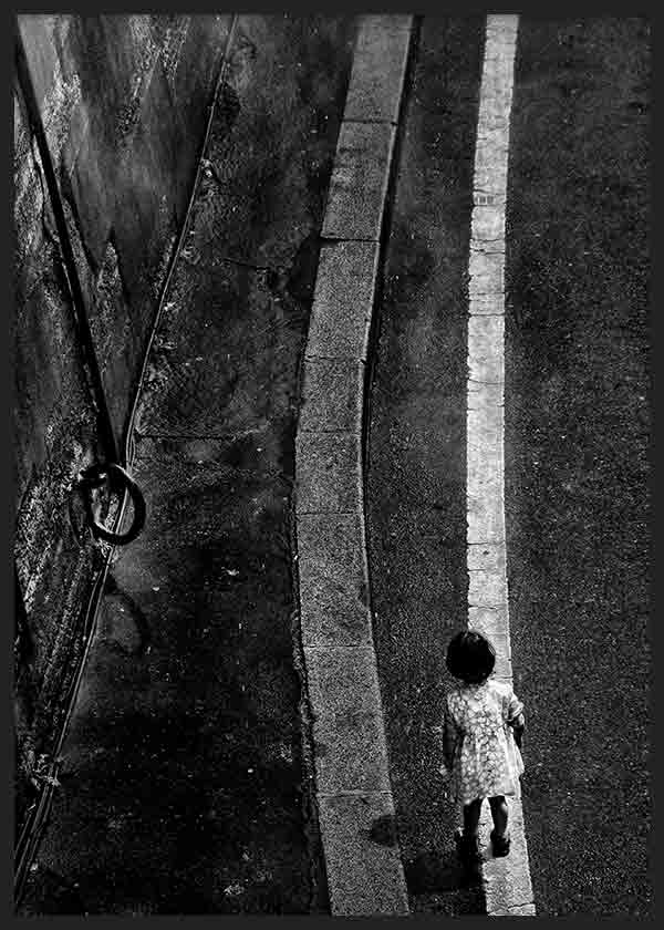 Tableau de scène urbaine en noir et blanc avec personne solitaire marchant près d’une ligne blanche sur asphalte sombre, aux textures marquées et au style photographique contemporain. Disponible sur kudeko.com