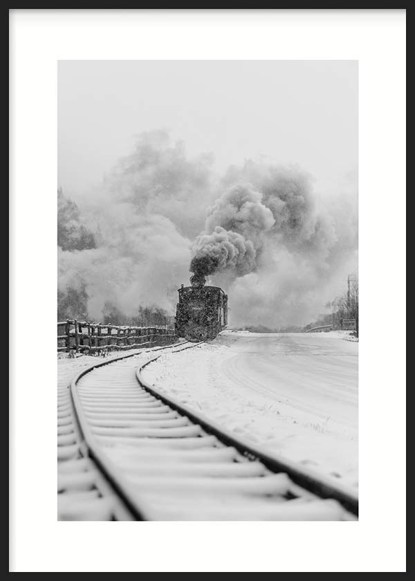 Wandbild mit Dampflokomotive auf verschneiten Gleisen, dichtem Rauch, winterlicher Landschaft in Weiß, Grau und Schwarz, in einem sachlichen fotografischen Stil. Erhältlich auf kudeko.com