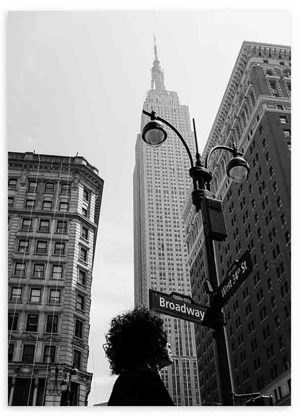 Tableau encadré d’une scène urbaine de New York en noir et blanc avec Empire State Building, lampadaires noirs, immeubles historiques, enseigne Broadway et silhouette au premier plan, dans un style ville. Disponible sur kudeko.com