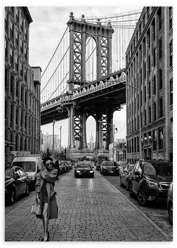 Quadro de rua urbana a preto e branco com grande ponte suspensa, edifícios de tijolo, carros estacionados e figura feminina em primeiro plano, em estilo fotográfico cinematográfico. Disponível em kudeko.com