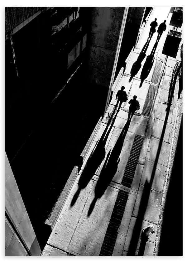 Cuadro de calle urbana en blanco y negro con peatones en movimiento, sombras alargadas, perspectiva cenital y estética fotográfica de alto contraste. Disponible en kudeko.com