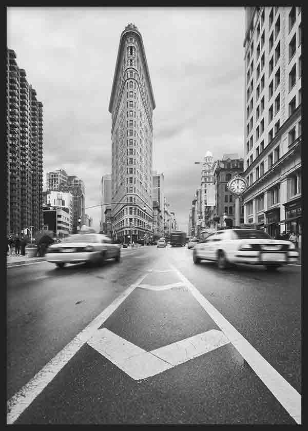 Gerahmtes Wandbild einer urbanen Allee in Schwarz-Weiß mit dreieckigem Hochhaus, fahrenden Autos, zentraler Perspektive und fotografischem Architekturstil. Erhältlich auf kudeko.com