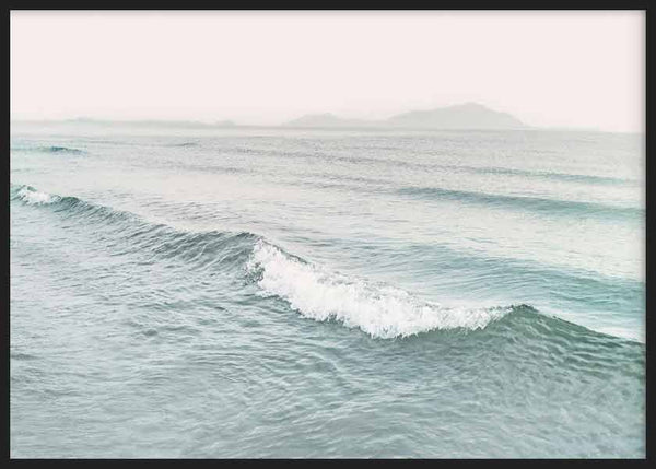 Cuadro horizontal de olas suaves en mar azul verdoso con espuma blanca, horizonte brumoso, montañas lejanas y estilo fotográfico sereno. Disponible en kudeko.com