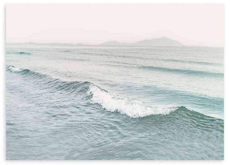 Horizontales Wandbild mit sanften Wellen auf blaugrünem Meer, weißem Schaum, dunstigem Horizont, fernen Bergen und ruhigem fotografischem Stil. Erhältlich auf kudeko.com